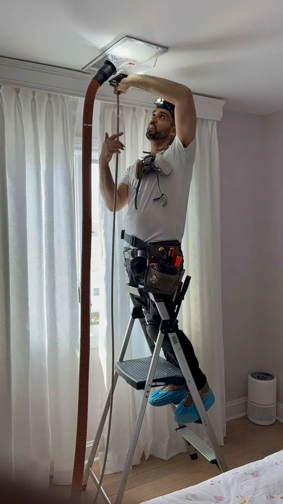 Professional air duct cleaning technician vacuuming ceiling vent in Nassau County home